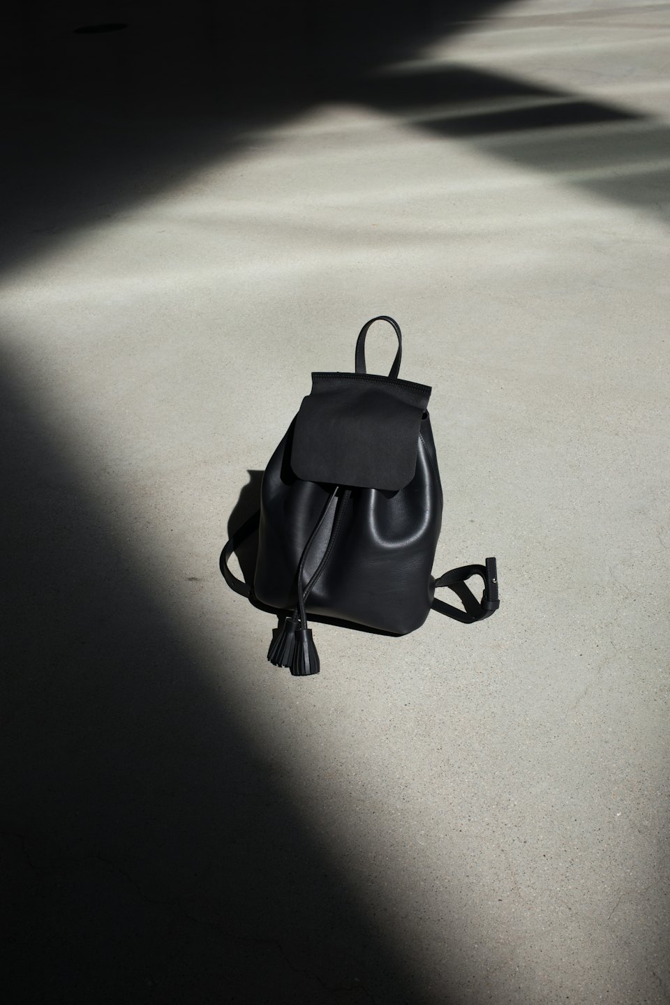 Black leather drawstring backpack with tassels on concrete.
