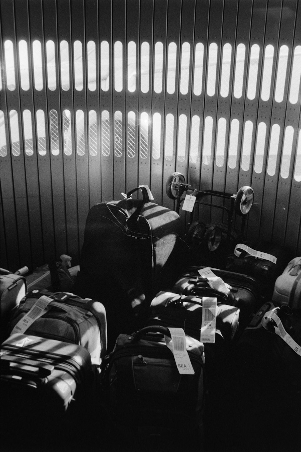 Various suitcases and backpacks piled against a metal wall.